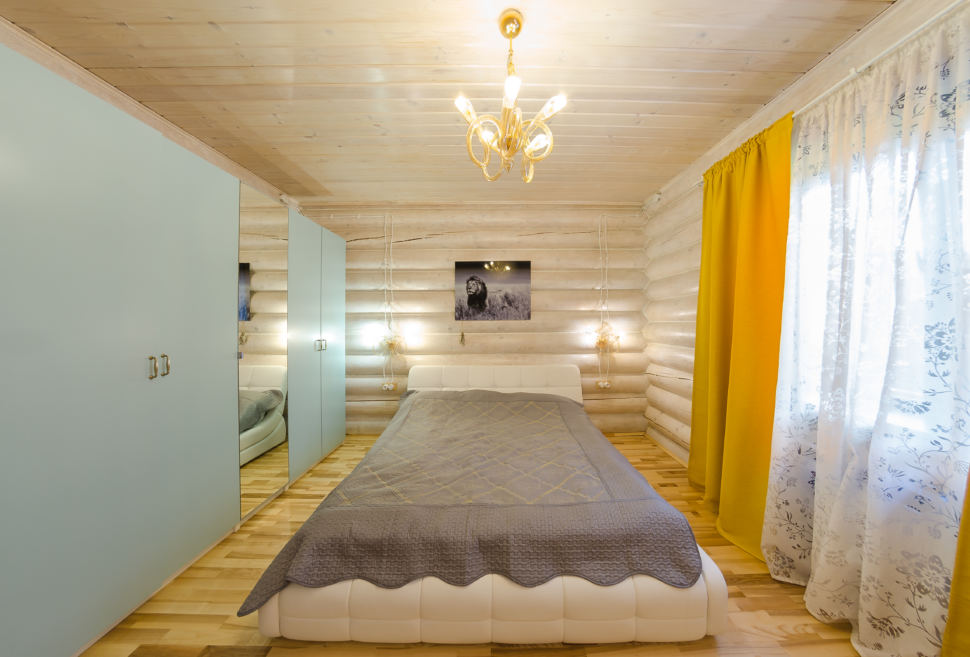 дизайн спальни в теплых тонах, желтые портьеры, текстиль серого цвета, брус, шкаф, подвесные светильники