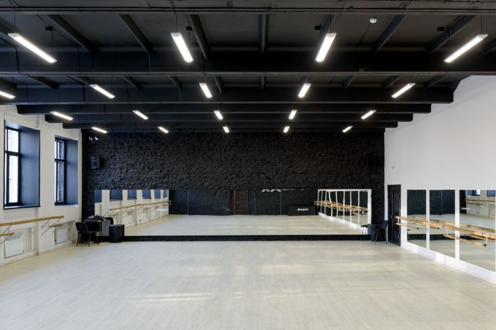 Фотография интерьера танцевального зала 210 кв.м, белый логотип, зеркала, черный окрашенный кирпич, черный потолок, подвесные светильники, двери, стол
