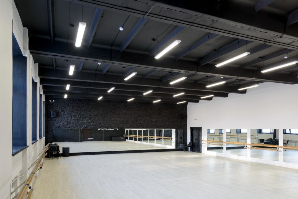 Фотография интерьера танцевального зала 210 кв.м, белый логотип, зеркала, черный окрашенный кирпич, черный потолок, подвесные светильники, двери, балки