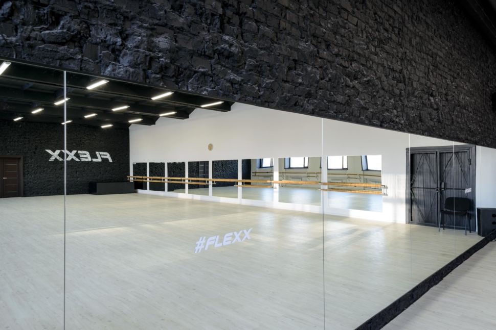Фотография интерьера танцевального зала 210 кв.м, белый логотип, зеркала, черный окрашенный кирпич, черный потолок, подвесные светильники, двери, стул